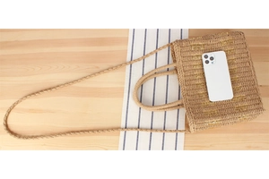 Flat lay of a woven straw beach bag with gold metallic accents on a light wood backdrop