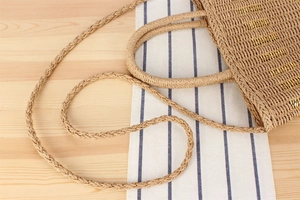 Detail of woven straw bag with gold thread accents and braided handles on wood surface
