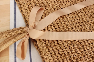 Detail of hand-woven straw bag with champagne pink ribbon bow and natural fiber texture