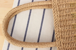 Detail of hand-woven straw tote bag with gold embroidery and round woven handles