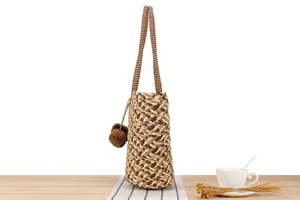 Detail of woven straw bucket bag with diamond texture and brown pompom charms
