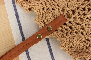 Close-up of woven straw tote bag detailing brown leather straps and metal rivets