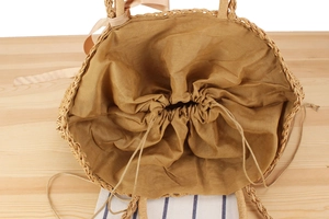 Detail view of woven straw bag with drawstring cotton lining and silk bow handle