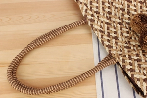 Close-up of woven paper straw tote bag with brown pom-pom details and lattice pattern