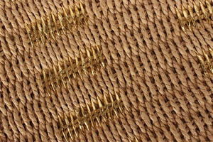 Macro shot of brown woven texture with interlaced gold metallic threads on women's beach bag