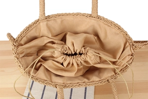 Detail view of woven straw beach bag featuring beige fabric drawstring liner and spacious interior