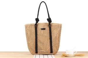 Detail of handwoven straw bag featuring black rope handles and elegant leather patch decoration
