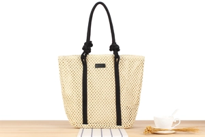 Close-up of a large capacity straw woven tote bag with black rope handles on wood surface