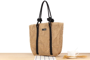 Detail of straw woven tote bag featuring black rope handles and minimal leather patch
