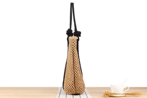 Detailed side view of handmade woven beach bag with hollow knit texture and black rope handles