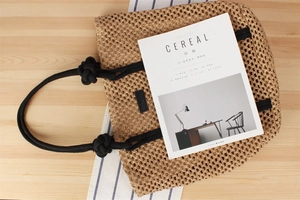 Detail of woven straw tote bag texture and black rope handle on a wooden table