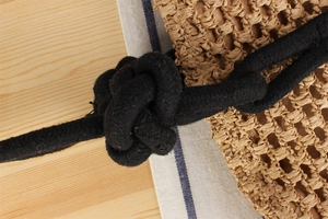 Detail of the knotted black cotton handle on a textured woven straw beach tote bag