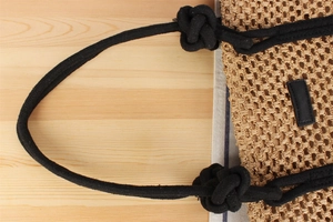 Detail of woven straw handbag featuring black knotted rope handles and rustic texture