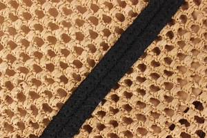 Close-up of straw beach bag featuring beige hollow woven texture and black strap