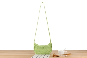 Dettaglio di una borsa a tracolla in paglia intrecciata verde chiaro su tavolo in legno