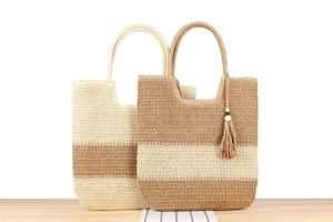 Detalle de bolsos tote de paja tejida con rayas y borla sobre una mesa de madera