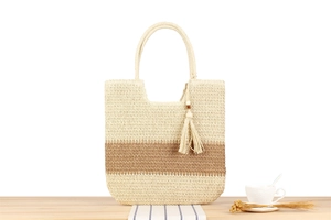 Detalle del bolso de paja tejida con rayas beige y marrones y adorno de borla