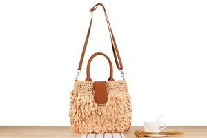 Detail of woven straw bag with fringe leaf pattern and brown leather handle