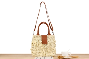 Detail of cream woven paper rope bag with fringe texture and brown leather straps