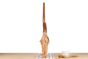 Side view of beige woven shoulder bag with long fringes and brown leather handles
