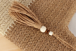 Detalle macro de un bolso tote de paja bicolor con borlas de rafia y cuentas de madera