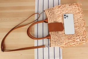 Detail of woven straw tote bag showing large capacity with leather straps and smartphone