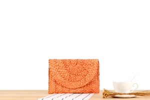 Detail of handmade orange corn husk woven clutch bag on a rustic wooden table setup