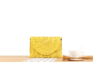 Detail of yellow handmade corn husk envelope clutch on wooden surface for beach vacations