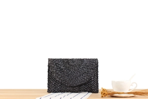 Detail shot of a black corn husk woven envelope clutch on a rustic wooden table surface