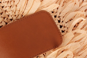 Close-up of brown leather texture and stitching detail on a hand-woven beach bag