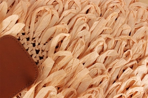 Macro detail of beige woven paper rope bag featuring a premium brown leather patch