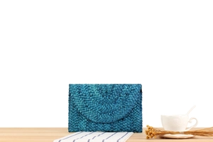Detail of blue woven corn husk clutch bag on a wooden table with casual decor