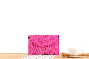 Detail of rose red corn husk woven clutch bag with V-shaped texture on a wooden desk