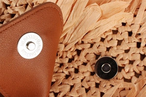 Detail of brown leather flap with silver magnetic clasp on woven straw beach bag