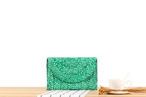 Detail of handmade corn husk woven clutch bag in green on a rustic wooden table
