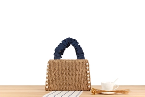 Detail of straw woven handbag with pearl trim and blue pleated satin handles on table