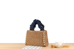 Detail of straw woven handbag featuring pearl side trim and navy blue ruffled handles