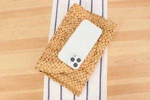 Macro detail of natural handmade corn husk woven clutch bag next to a smartphone