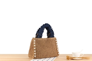 Detail of hand-woven straw bag with pearl trim and blue ruffled handles for summer