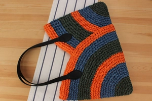 Detail view of colorful woven tote bag with wavy stripes and black leather handles