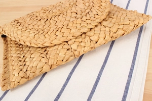 Detail of handcrafted corn husk woven envelope clutch on a wooden table with striped linen