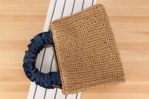 Detailed top view of a woven straw tote bag featuring navy blue ruffled satin handles