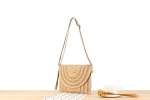 Detalle del bolso de paja tejida beige con textura y correa ajustable en color café