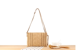 Detalle de bolso bandolera de paja hecho a mano con correa marrón sobre una mesa