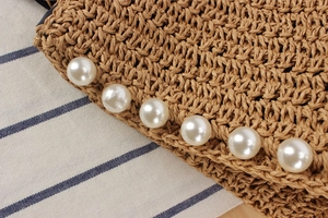 Macro detail of hand-woven straw bag featuring large white pearl accents on lace ribbon