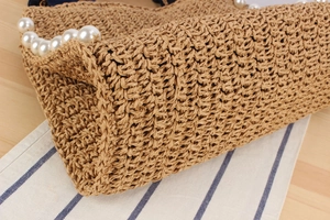 Detail shot of handwoven straw bag featuring large white pearls and natural cord texture