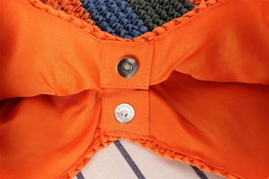 Detail of the silver magnetic clasp and orange fabric lining on the woven handbag