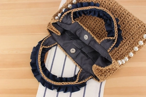Detail view of woven straw bag featuring pearl trim and magnetic snap closure