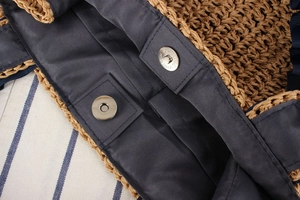 Detail view of woven straw bag showing magnetic metal snap closure and fabric lining