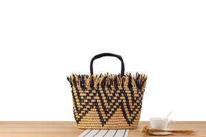 Detail of straw woven beach bag featuring black wave patterns and fringe tassels